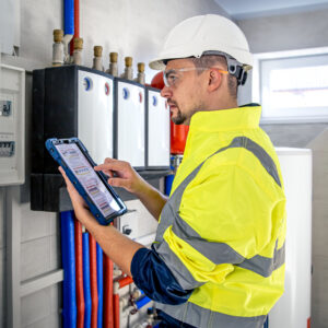 Man, an electrical technician in uniform working in a switchboard with fuses. Installation and connection of electrical equipment. Professional uses a tablet.