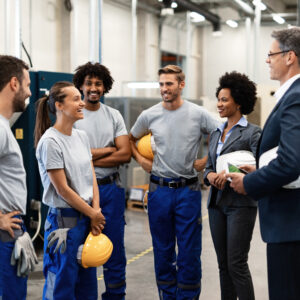 Young happy female worker and her colleagues communicating with company managers in a factory.